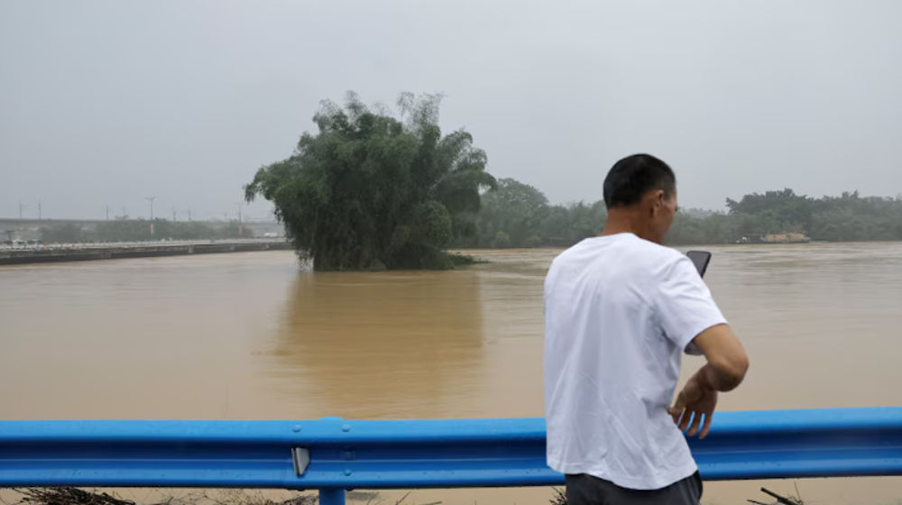 Seorang warga menggunakan ponselnya saat dia berdiri di dekat sungai yang banjir setelah hujan lebat di Qingyuan, provinsi Guangdong, China 22 April 2024. 