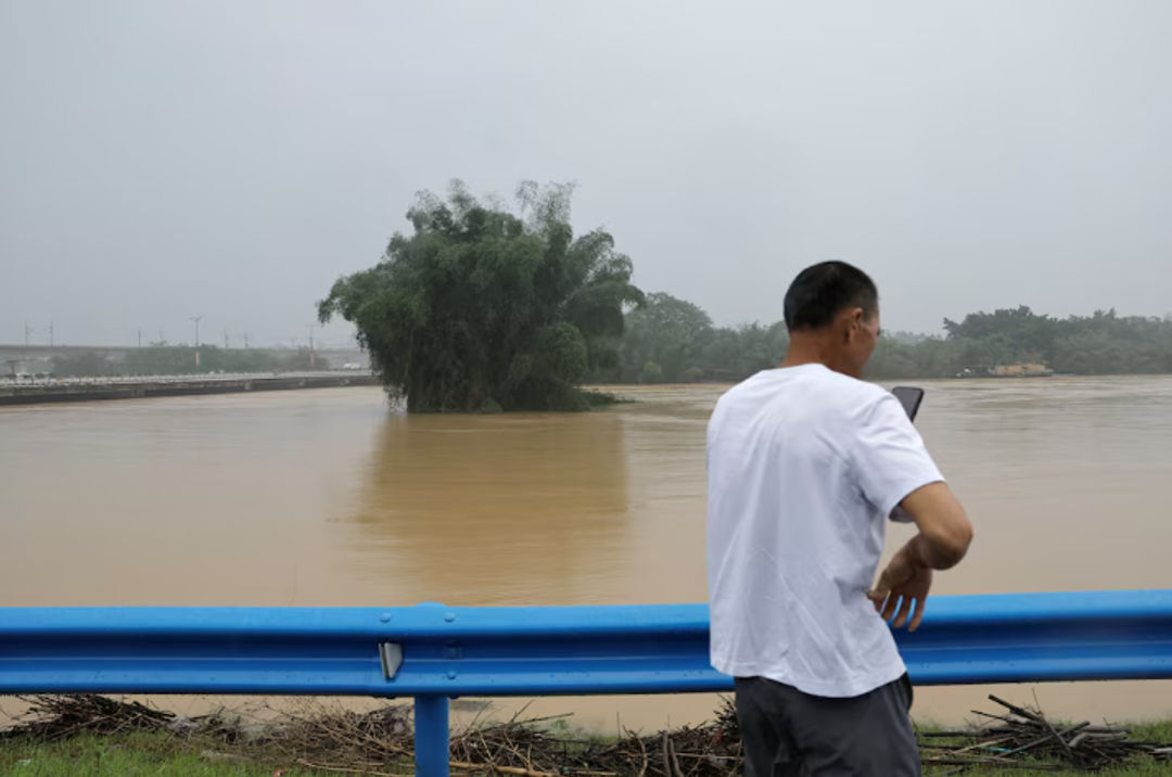 Seorang warga menggunakan ponselnya saat dia berdiri di dekat sungai yang banjir setelah hujan lebat di Qingyuan, provinsi Guangdong, China 22 April 2024. (Reuters/Tingshu Wang)