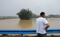 Seorang warga menggunakan ponselnya saat dia berdiri di dekat sungai yang banjir setelah hujan lebat di Qingyuan, provinsi Guangdong, China 22 April 2024. 