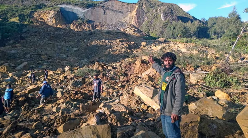 Warga memanjat batu-batu besar yang berserakan di antara batang pohon dan puing-puing yang ditinggalkan oleh tanah longsor.
