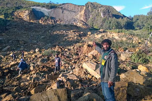 Warga memanjat batu-batu besar yang berserakan di antara batang pohon dan puing-puing yang ditinggalkan oleh tanah longsor.