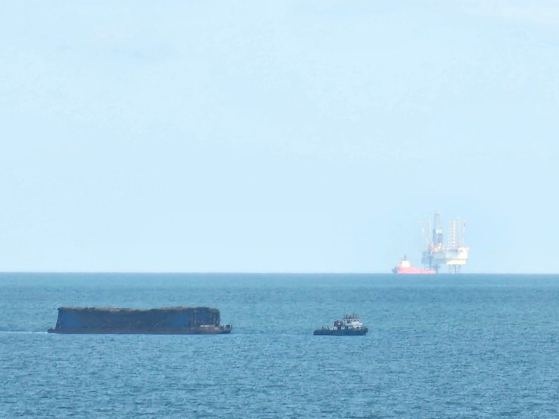 Sebuah tongkang batubara melintas di Teluk Balikpapan. Dari kejauhan terlihat lapangan pengeboran lepas pantai yang dioperasikan ENI Indonesia. Tahun ini perusahaan minyak asal Italia itu akan melakukan survei seismik 3D di Cekungan Kutai.