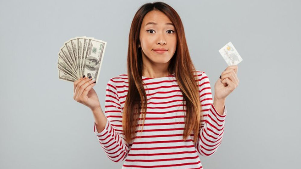 Perempuan memegang uang dan kartu kredit.