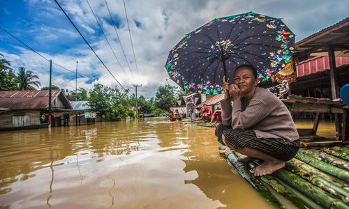 Seorang perempuan memegang payung menunggu dievakuasi tim penyelamat di atas rakit bambu di depan rumahnya yang terendam banjir di Desa Sungai Raya, Kabupaten Banjar, Kalimantan Selatan. Banjir yang disebabkan oleh curah hujan tinggi musiman dan pembukaan lahan besar-besaran untuk pertambangan kelapa sawit dan batu bara di Kalimantan Selatan.