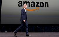 Jeff Bezos berdiri di depan logo Amazon, e-commerce raksasa Amerika Serikat.