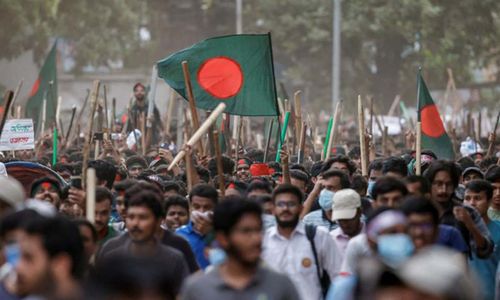 Para pengunjuk rasa merayakan di samping potret Perdana Menteri Sheikh Hasina yang dirusak setelah berita pengunduran dirinya, di Dhaka, Bangladesh.