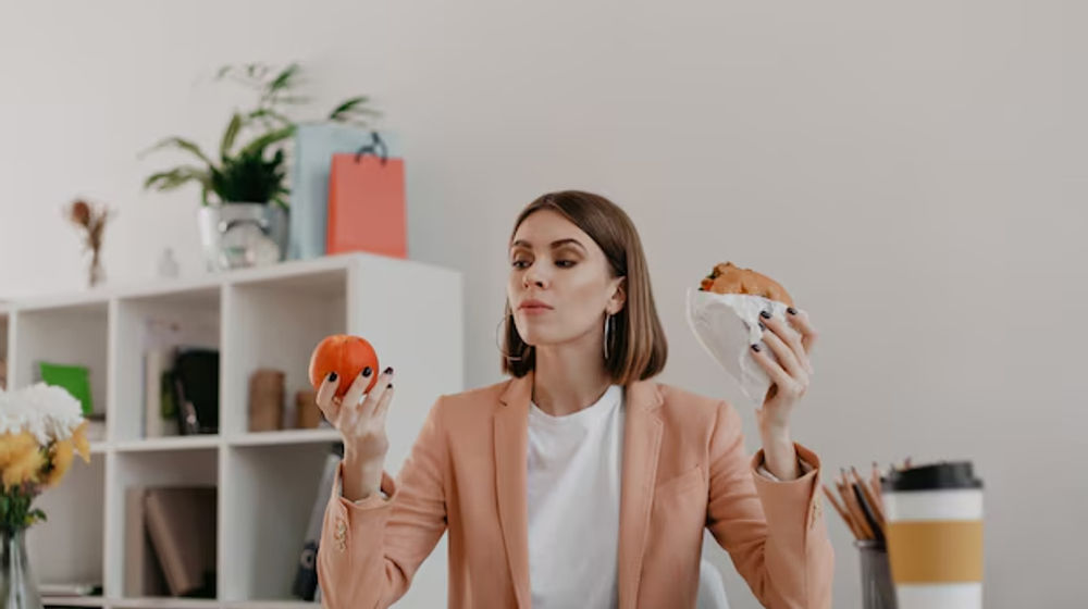 Ilustrasi wanita sedang makan camilan di meja kerja kantor.