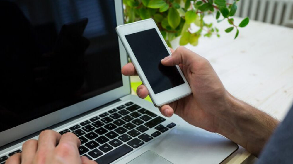 Ilustrasi orang memegang hp di depan laptop.