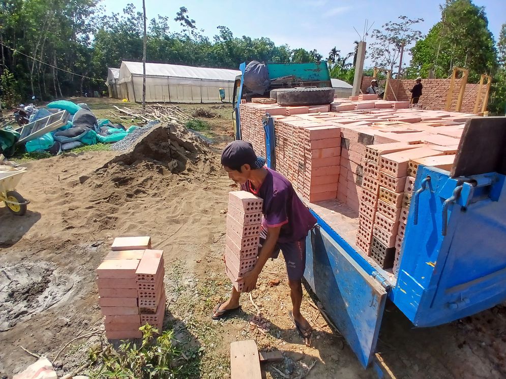 Pegawai menurunkan batu bata dari bak mobil truk yang telah dipesan pembeli di Banyuasin pada Kamis, 21 November 2024. 