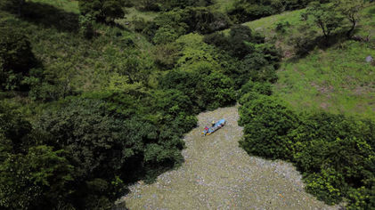 Warga berjalan di antara sampah saat bekerja dalam program yang didanai pemerintah Salvador untuk membersihkan waduk El Cerron Grande di Potonico, El Salvador, 14 September 2022.