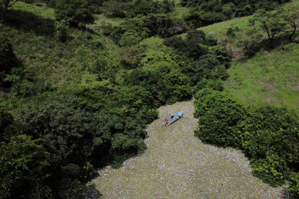 Warga berjalan di antara sampah saat bekerja dalam program yang didanai pemerintah Salvador untuk membersihkan waduk El Cerron Grande di Potonico, El Salvador, 14 September 2022.