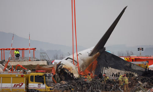 Orang-orang berdiri di dekat reruntuhan pesawat yang tergeletak di tanah setelah keluar landasan pacu dan jatuh di Bandara Internasional Muan, di Muan, Korea Selatan, 30 Desember 2024.