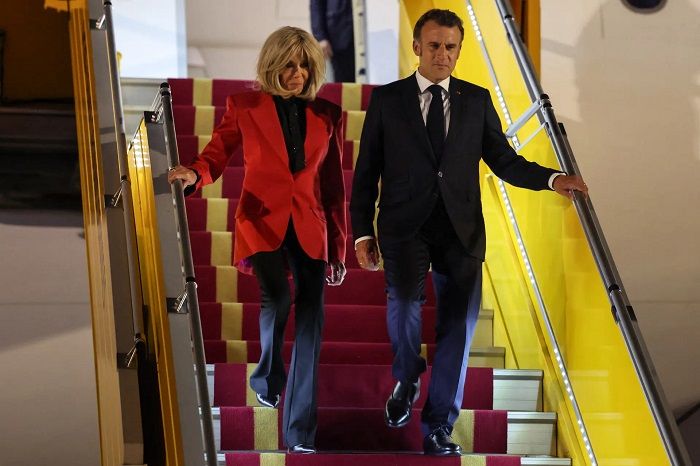 Emmanuel Macron dan Brigitte Macron berjalan bersama menuruni tangga pesawat.