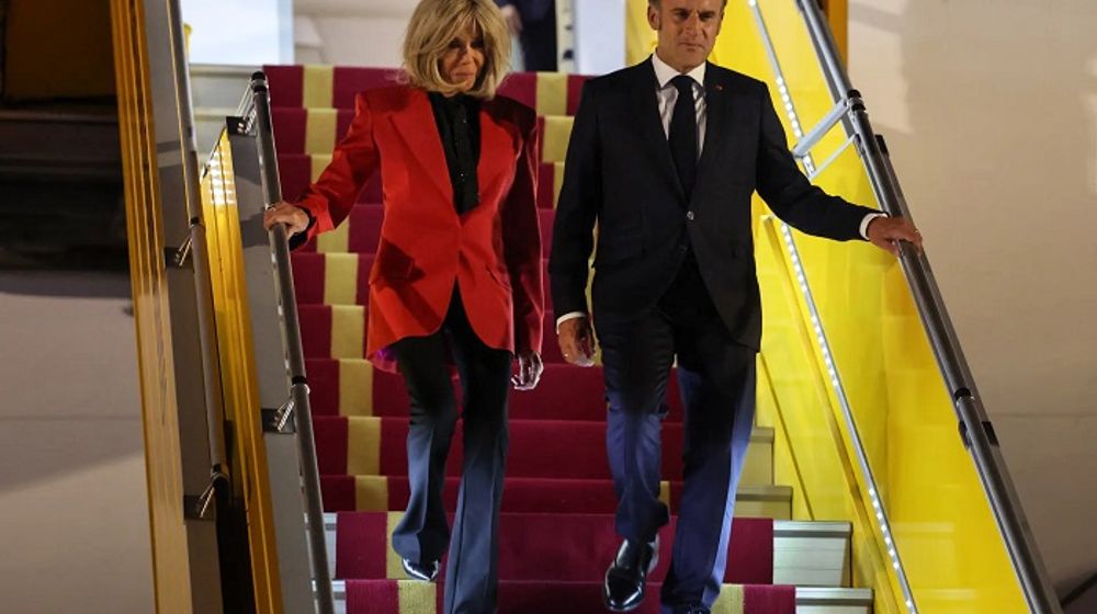 Emmanuel Macron dan Brigitte Macron berjalan bersama menuruni tangga pesawat.