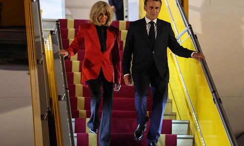 Emmanuel Macron dan Brigitte Macron berjalan bersama menuruni tangga pesawat.