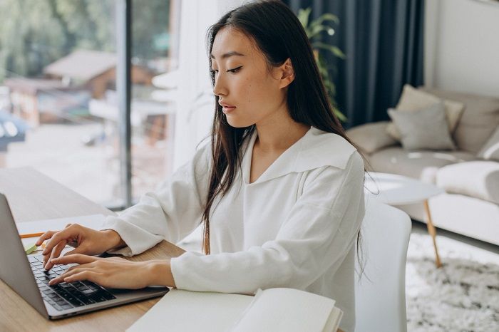 Ilustrasi wanita di rumah sedang mengerjakan sesuatu di laptopnya.