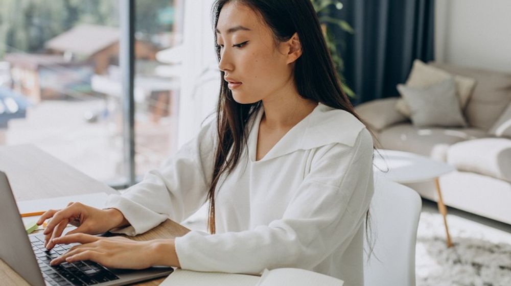 Ilustrasi wanita di rumah sedang mengerjakan sesuatu di laptopnya.