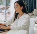 Ilustrasi wanita di rumah sedang mengerjakan sesuatu di laptopnya.