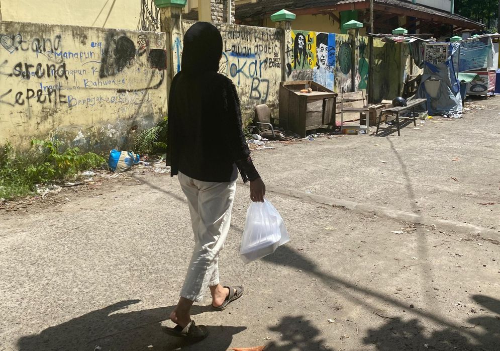 Seorang perempuan melintas dan membawa makanan dengan kemasan plastik bening
