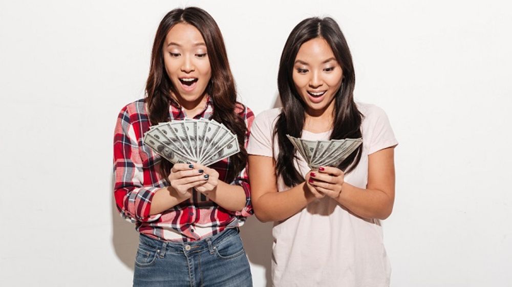 Ilustrasi dua orang wanita sedang memegang uang hasil tabungan.