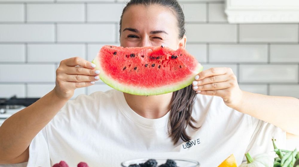 Wanita makan semangka di cuaca panas.