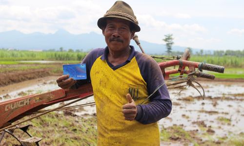 Petani memegang buku tabungan BRI di sawah sambil mengacungkan jempol setelah menerima bantuan BLTS Kesra.