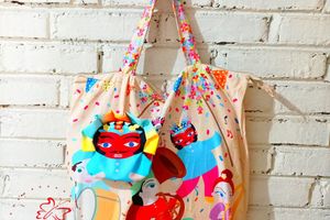 Tote bag bermotif ilustrasi budaya Betawi dengan karakter ondel-ondel dan musisi tradisional, digantung di dinding bata putih sebagai produk kerajinan Pundi Craft.