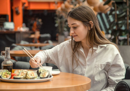 Wanita sedang menikmati sushi di tempat.