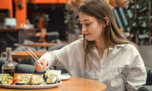 Wanita sedang menikmati sushi di tempat.