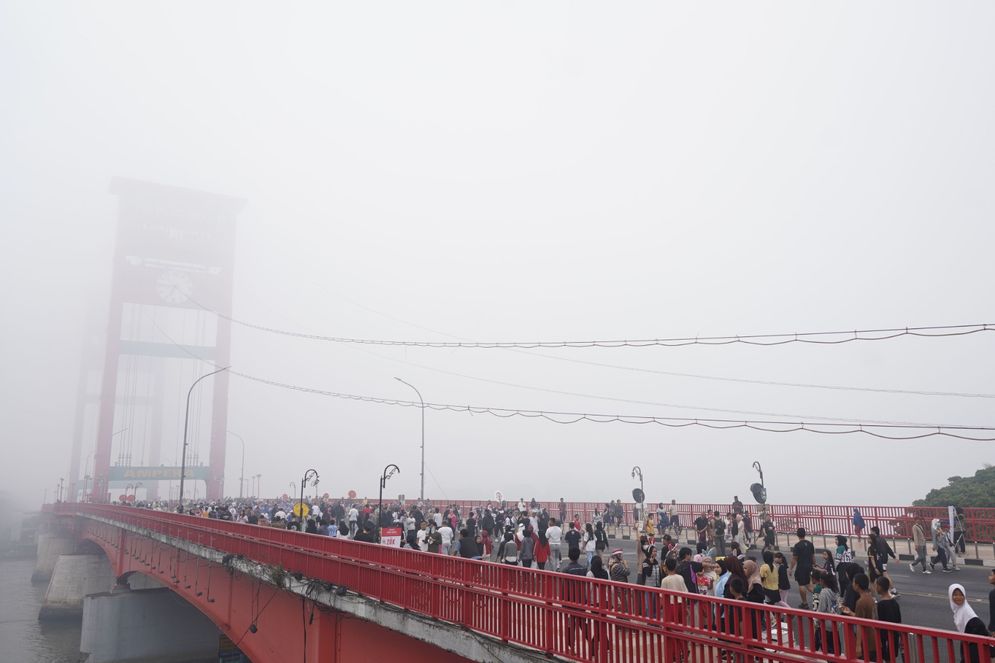 Warga beraktivitas di Jembatan Ampera yang tertutupi kabut asap di Palembang